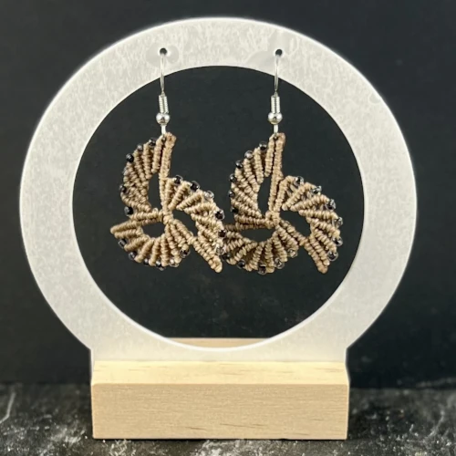 Boucles d’oreilles spirales beige clair en micro-macramé avec perles marron transparentes sur présentoir en bois.