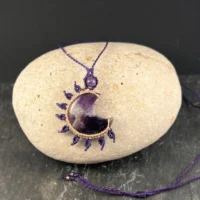 Collier en micro-macramé violet avec pendentif lune en améthyste posé sur une pierre